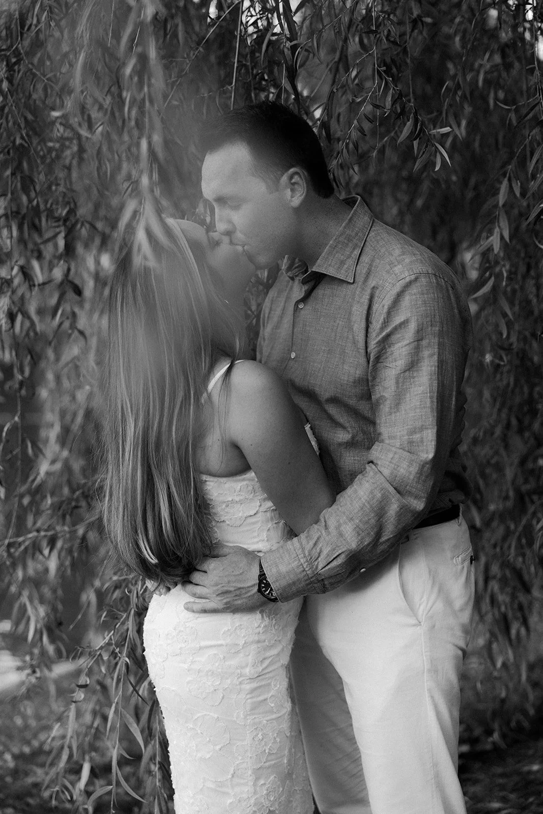 A man kissing his fiancee underneath a tree