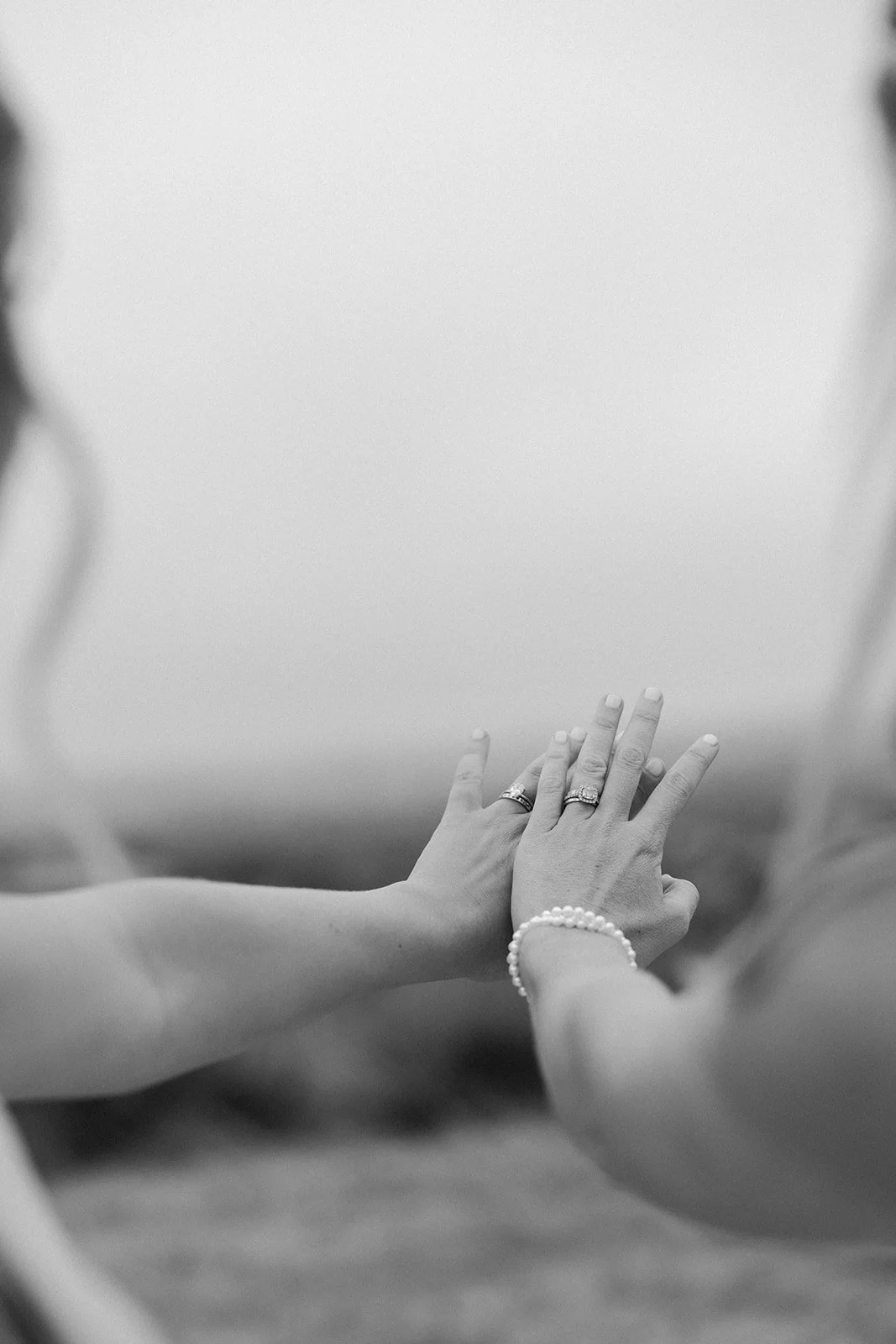 Two brides holding out their hands showing off their rings in a black and white wedding photo