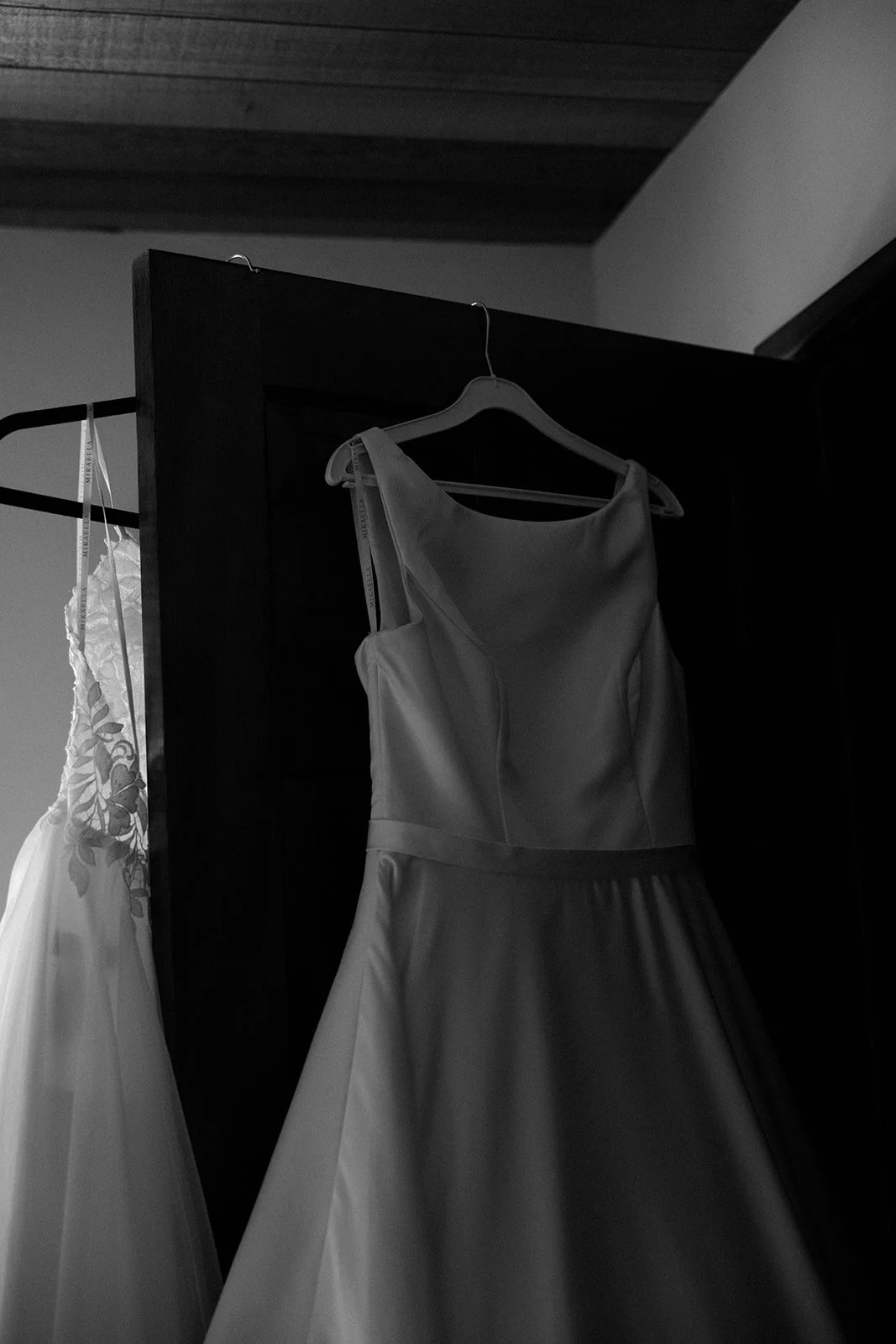 A black and white photo of two wedding dresses hanging 