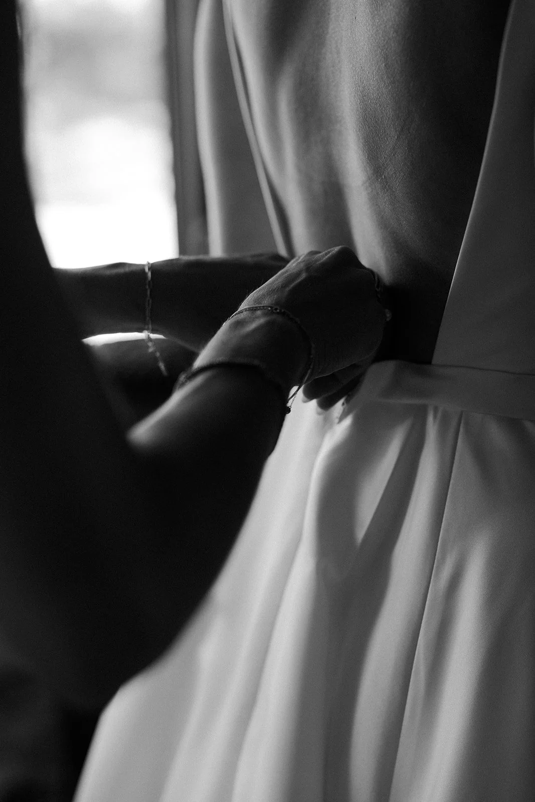 A bridesmaid helping a bride put on her wedding dress in documentary style wedding photography