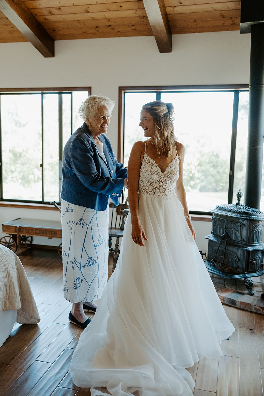 A bride laughing with her grandma, who is helping her put on her wedding dress, during documentary style wedding photography