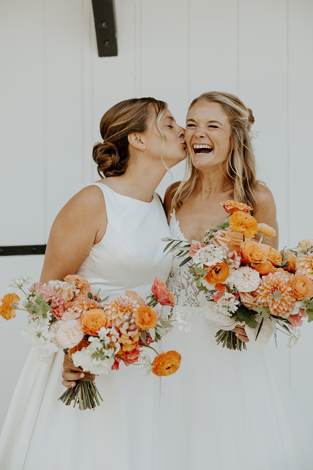 A bride kissing her wife on the cheek in a whimsical wedding