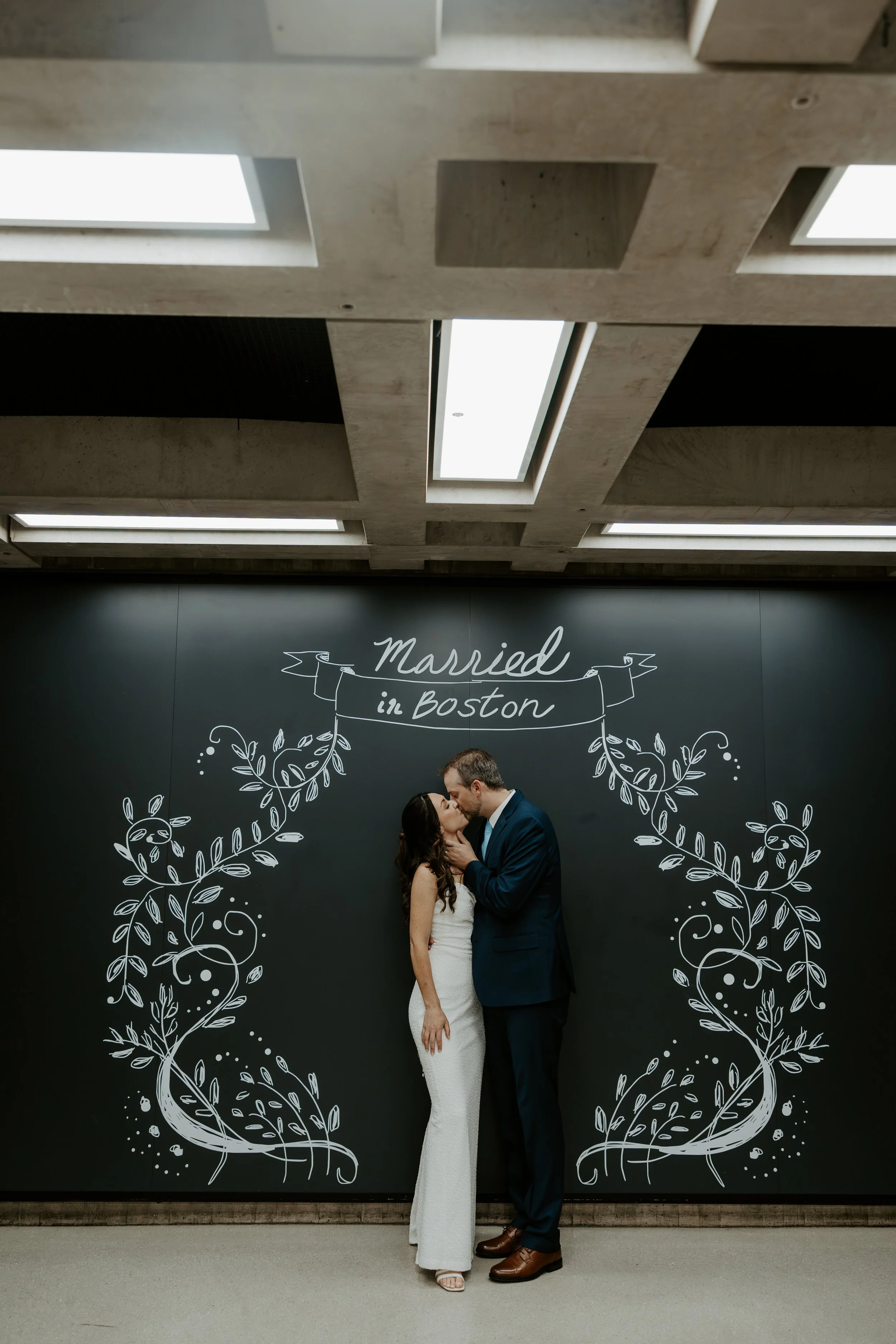 A couple kissing in front of a mural at their Boston City Hall wedding