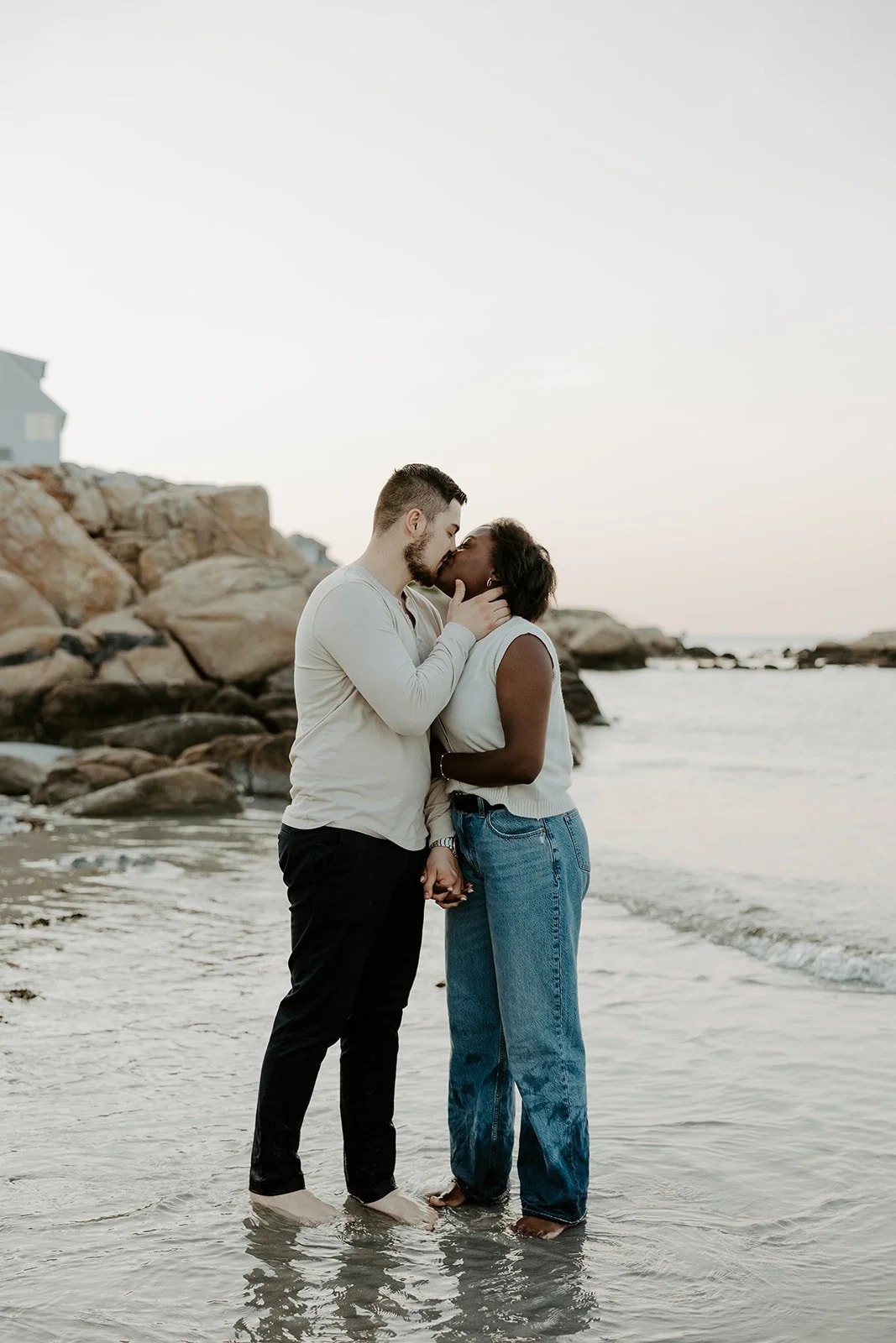 A couple kissing on the shoreline at their beach engagement photoshoot