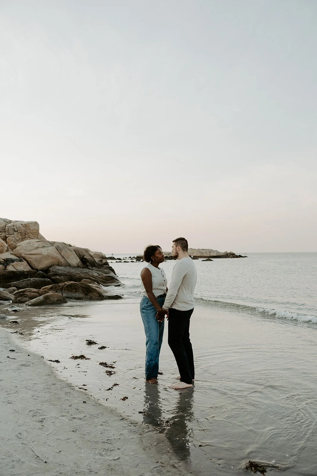 A couple standing holding hands on the shoreline of Wingaersheek beach
