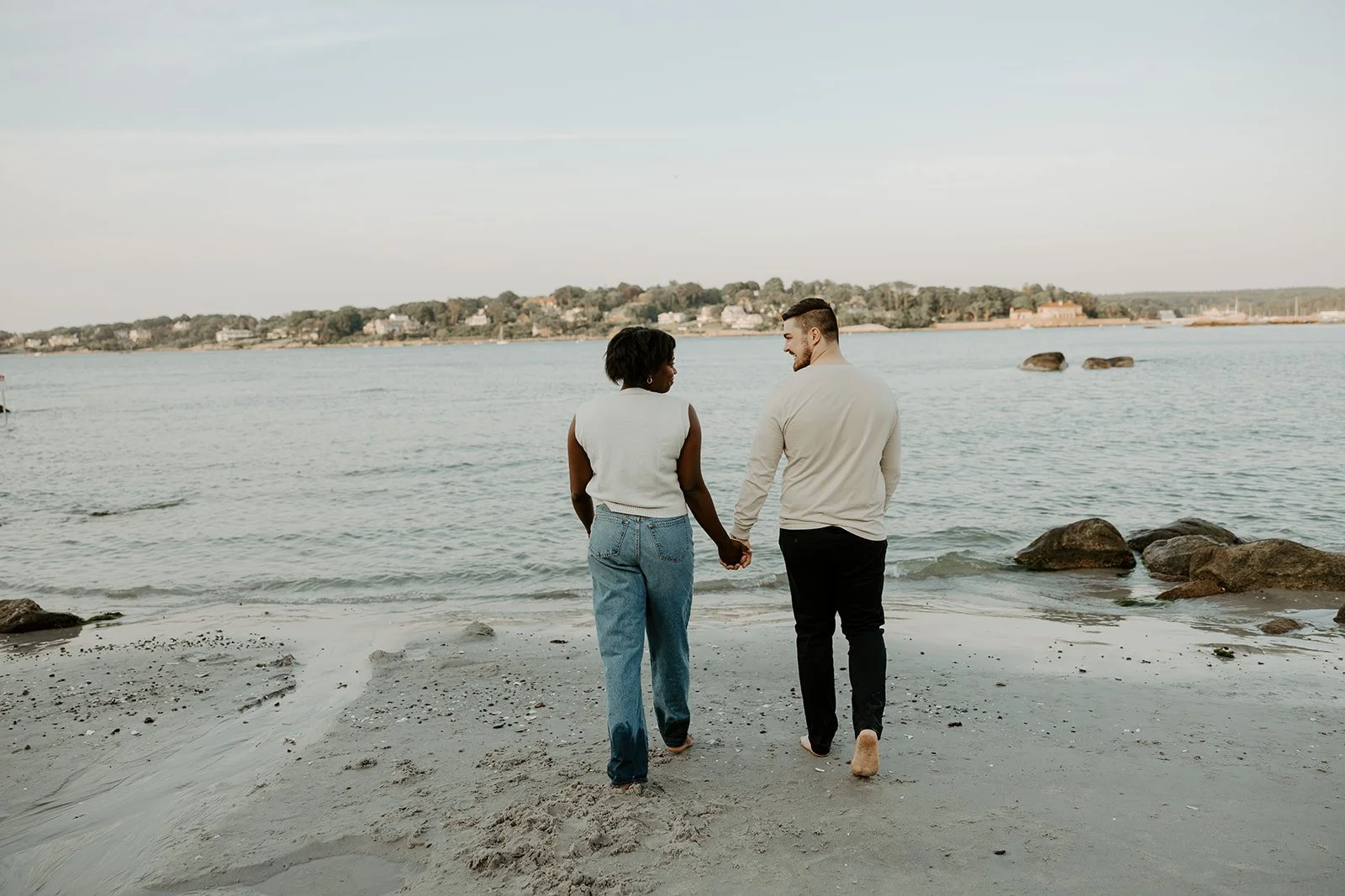 A couple holding hands and walking towards the ocean during engagement photos at Wingearsheek beach