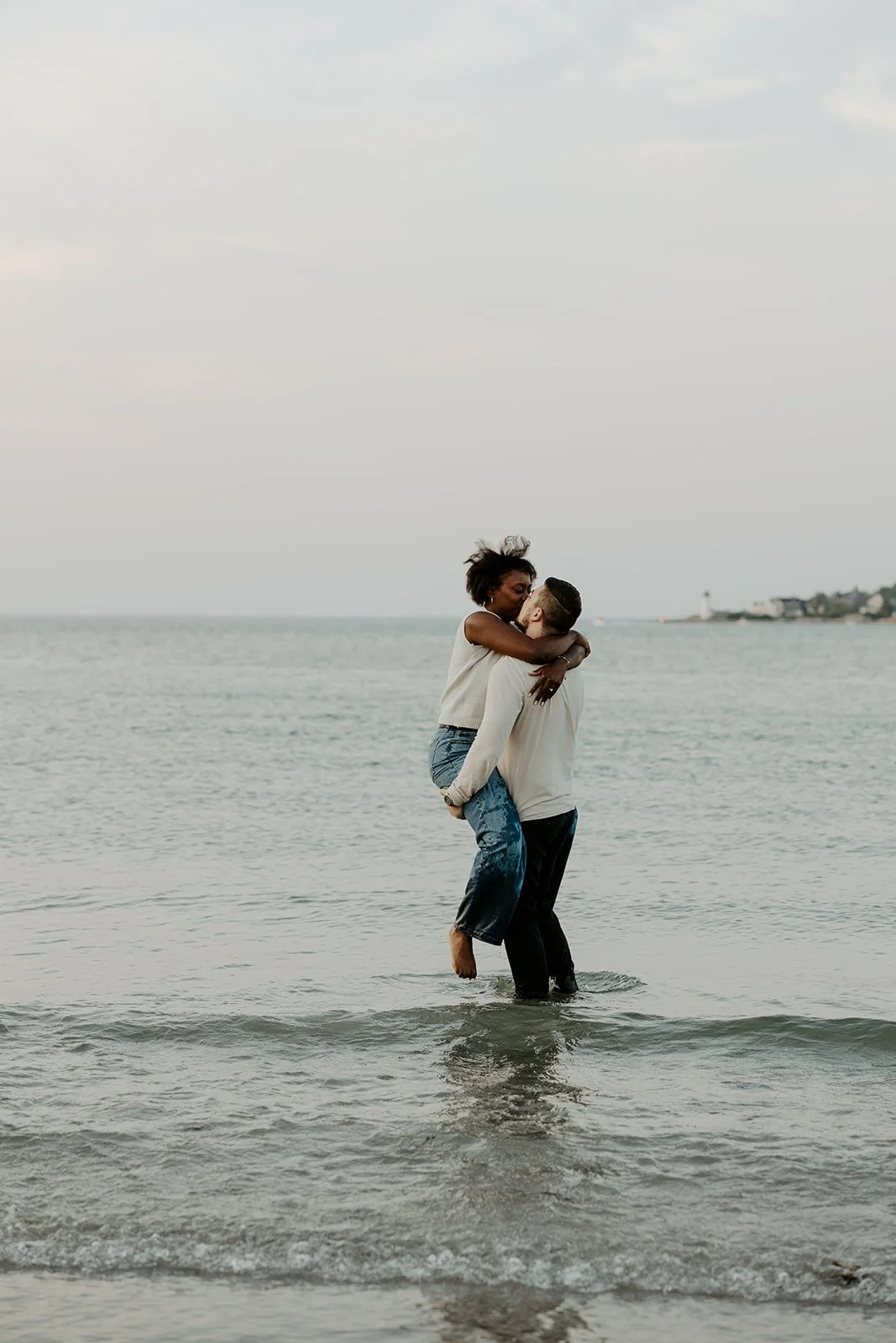 A man lifting up his fiancee in the ocean during their beach engagement photoshoot
