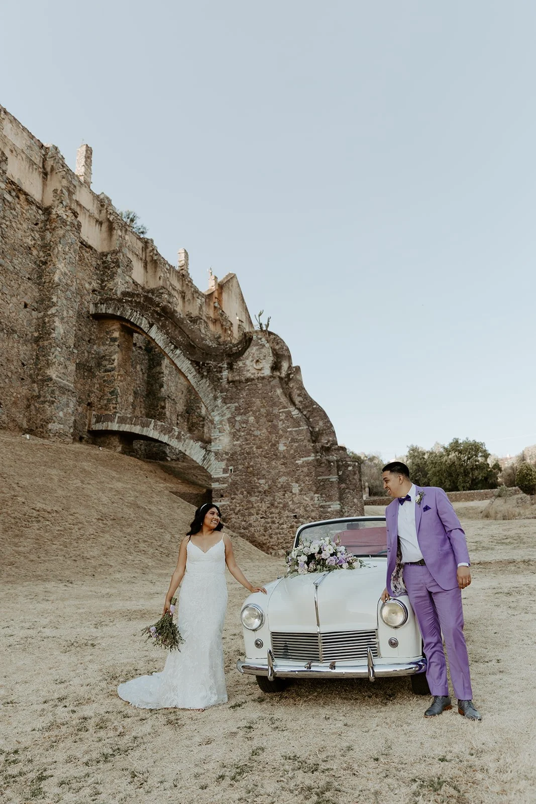 A couple posing with a vintage car at their MExico destination wedding