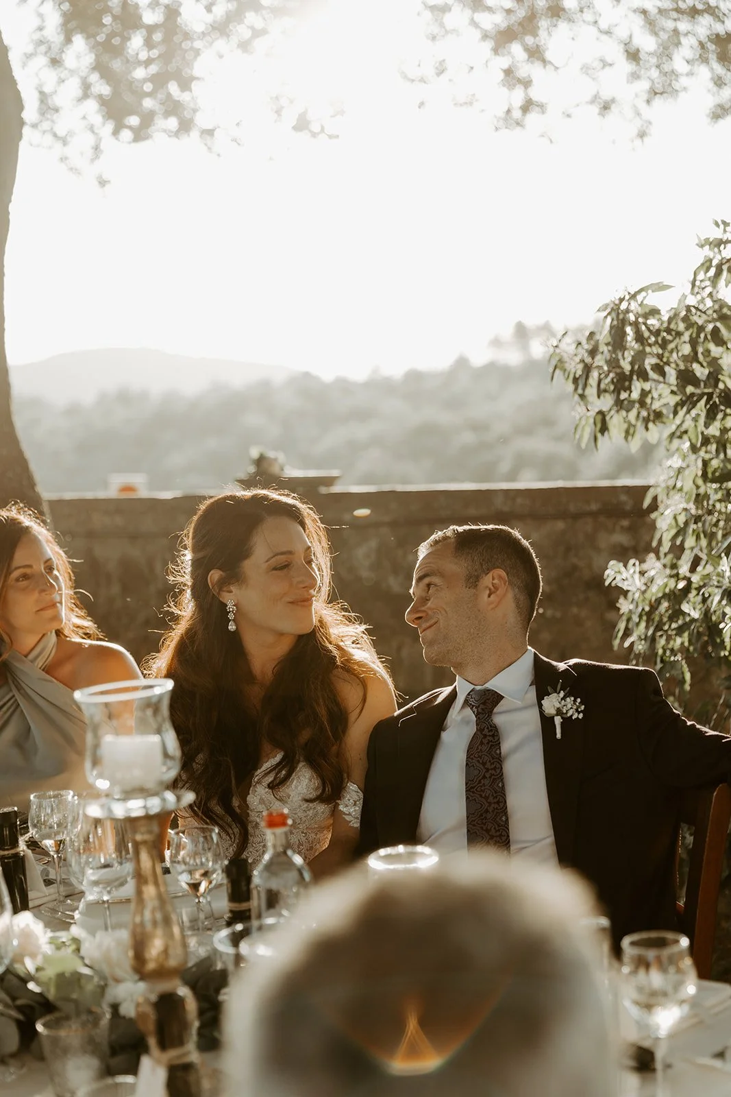A candid wedding photo of bride and groom smiling at each other during toasts