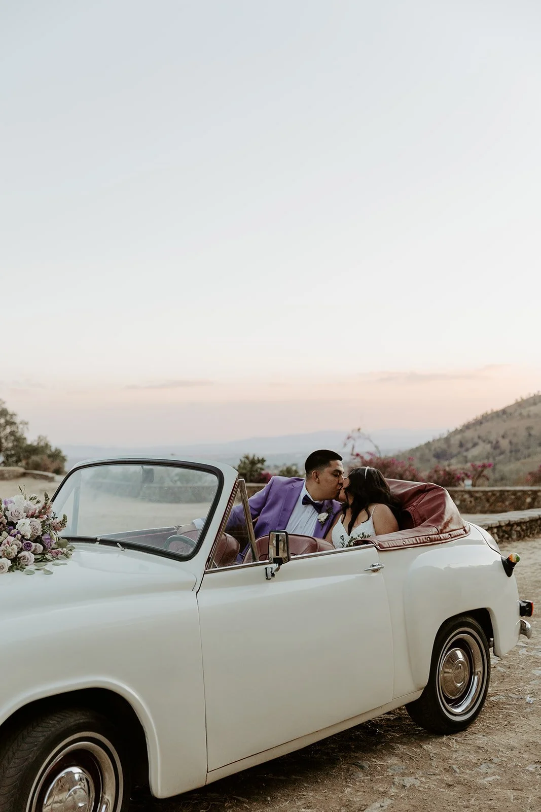 A couple kissing in a vintage car at their Mexico destination wedding