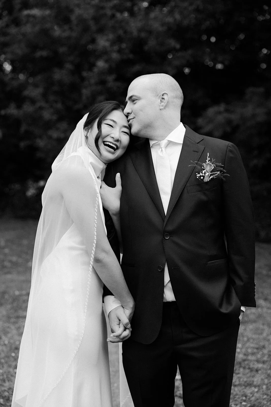 A groom kissing a bride on the forehead during wedding photos