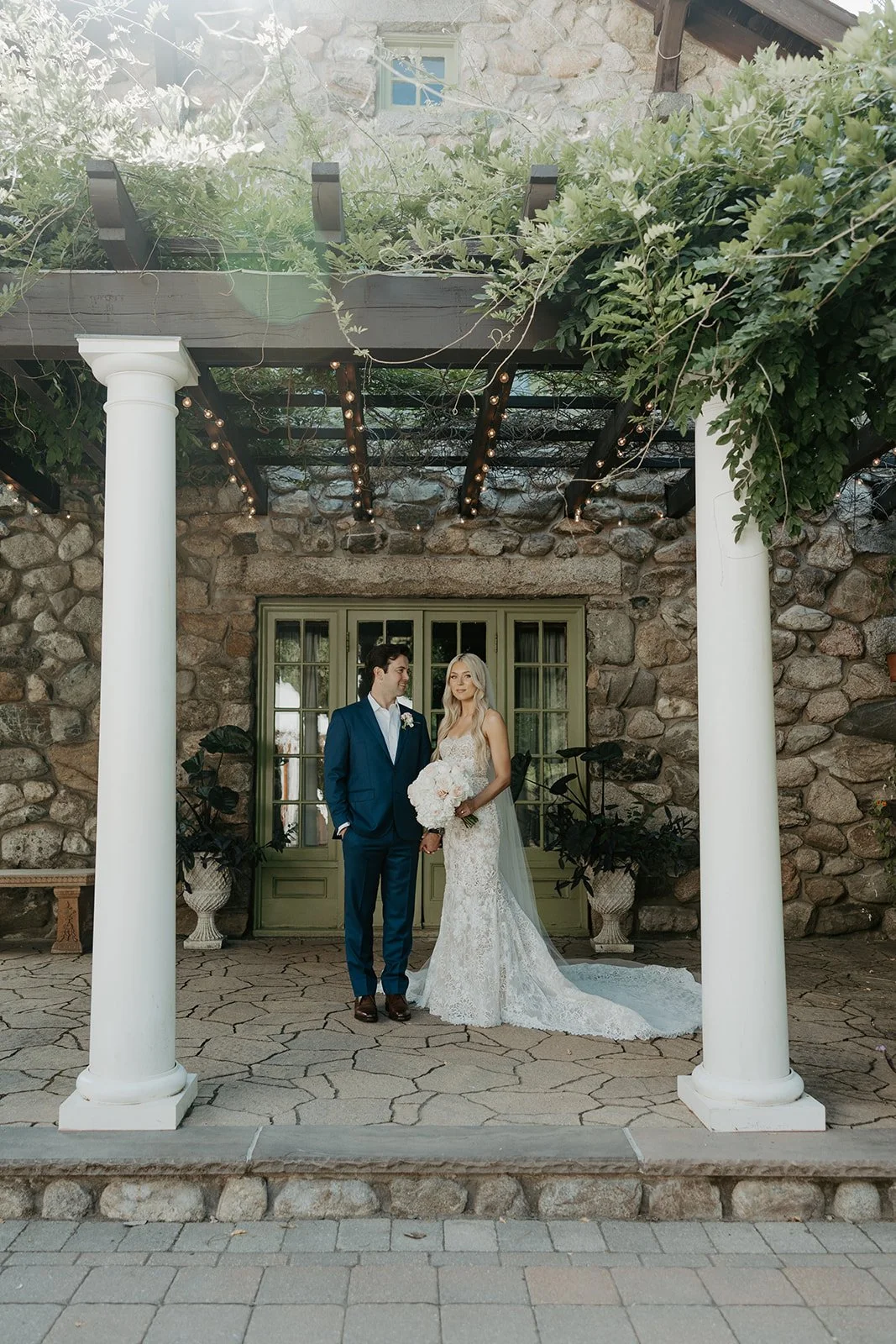 A bride and groom posing for wedding photos on the porch of a mansion
