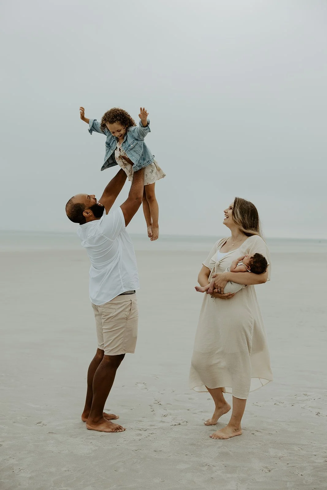 A dad tossing his daughter up in the air while a mother watches during a beach family photoshoot