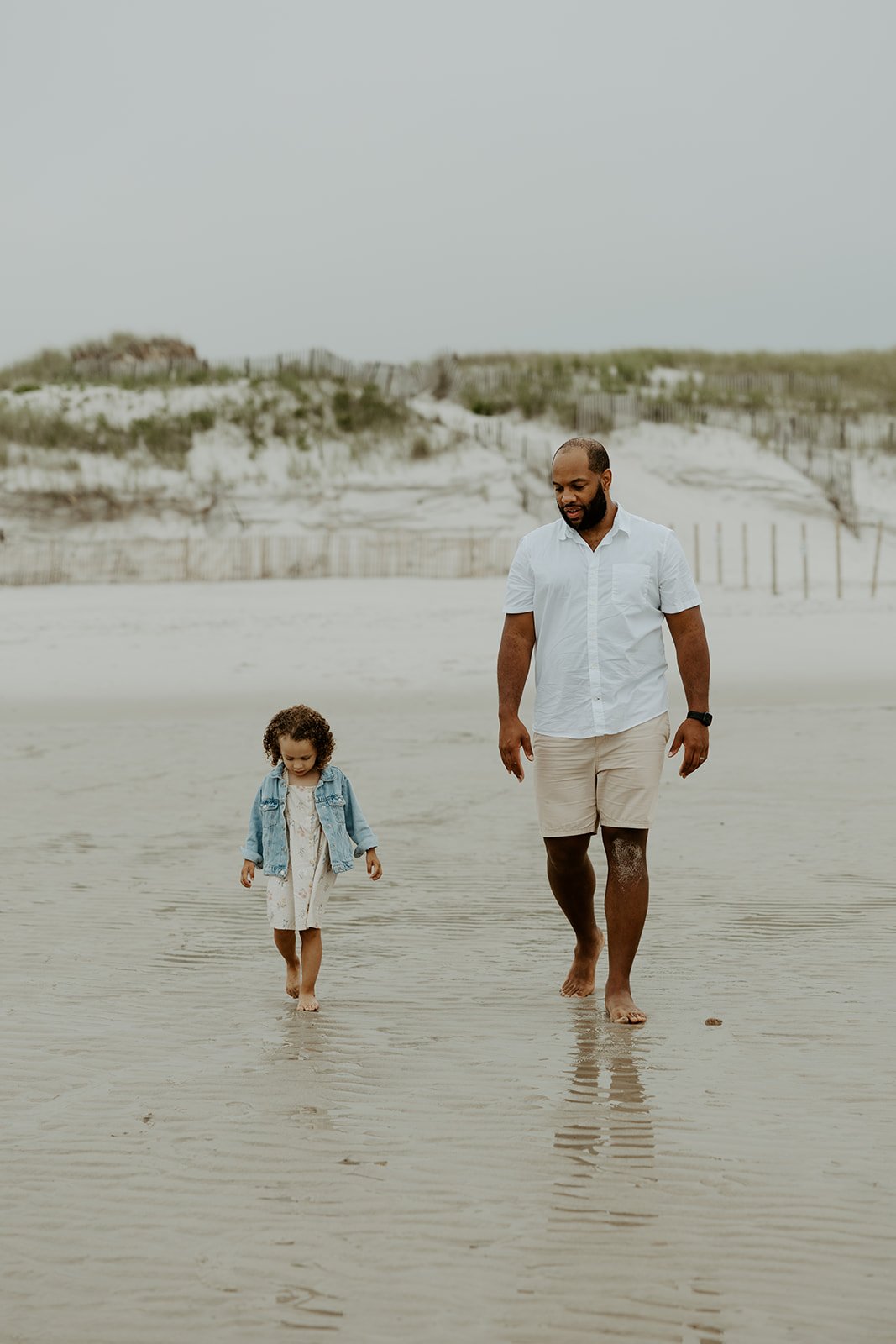 A dad and daughter walking on the shoreline during a beach family photoshoot