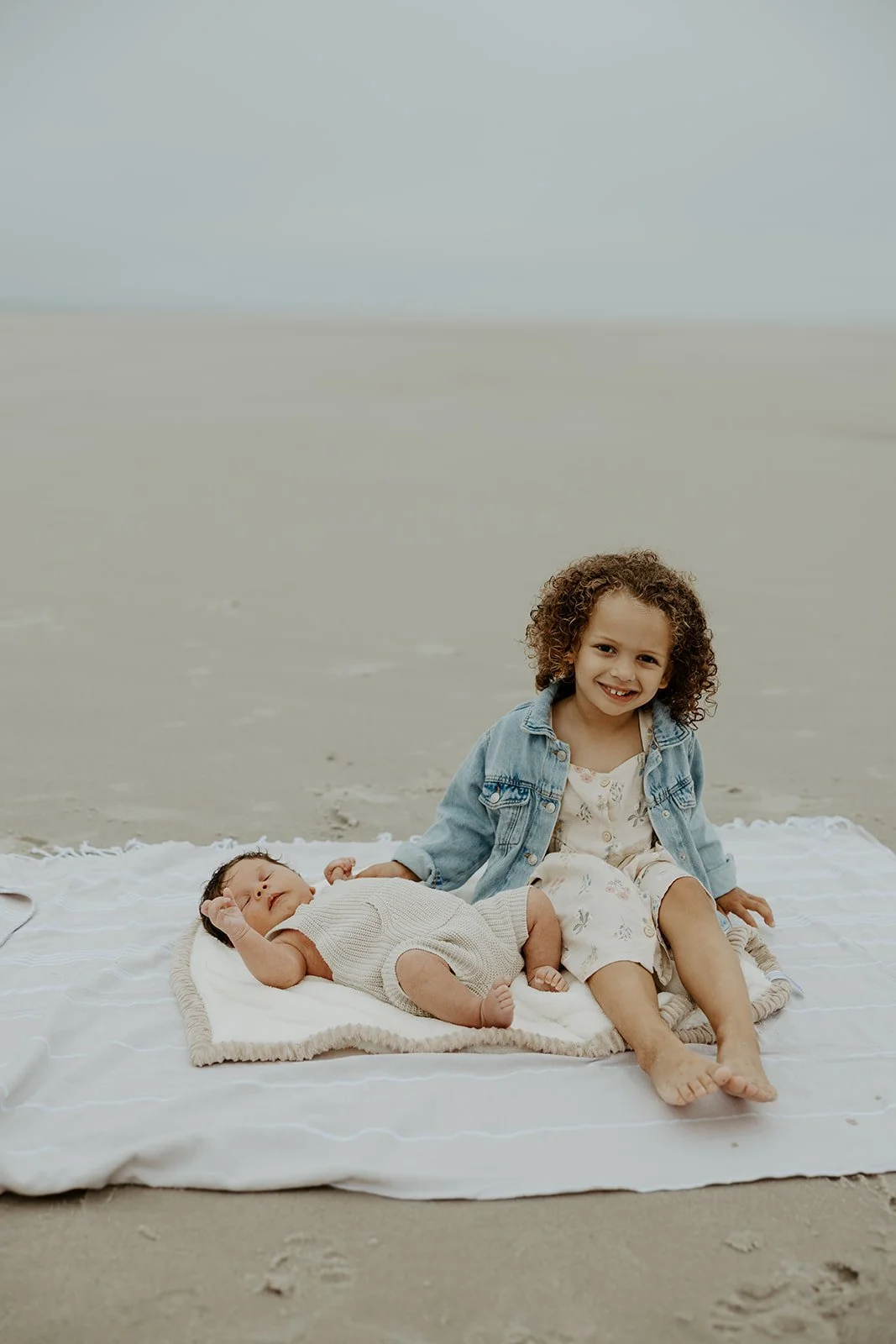 A little girl and her baby brther on a beach towel during a beach family photoshoot