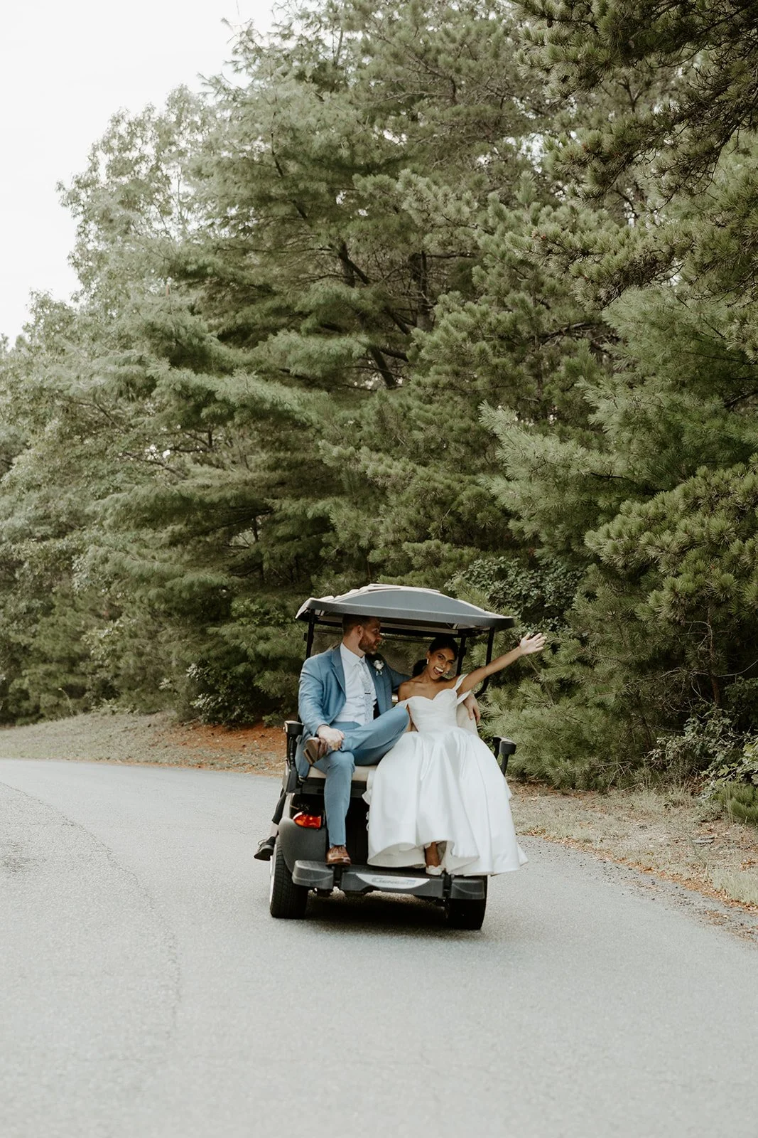 A bride and groom riding away on a golf cart