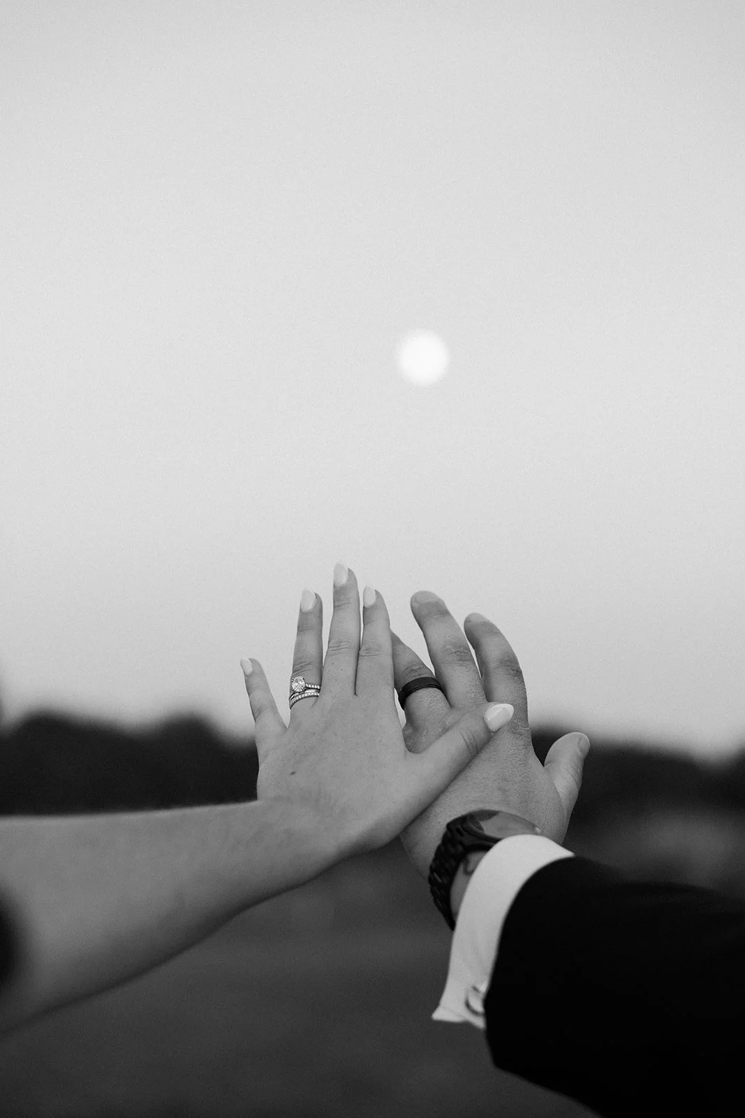 A bride and groom showing off their wedding rings with the moon behind their hands