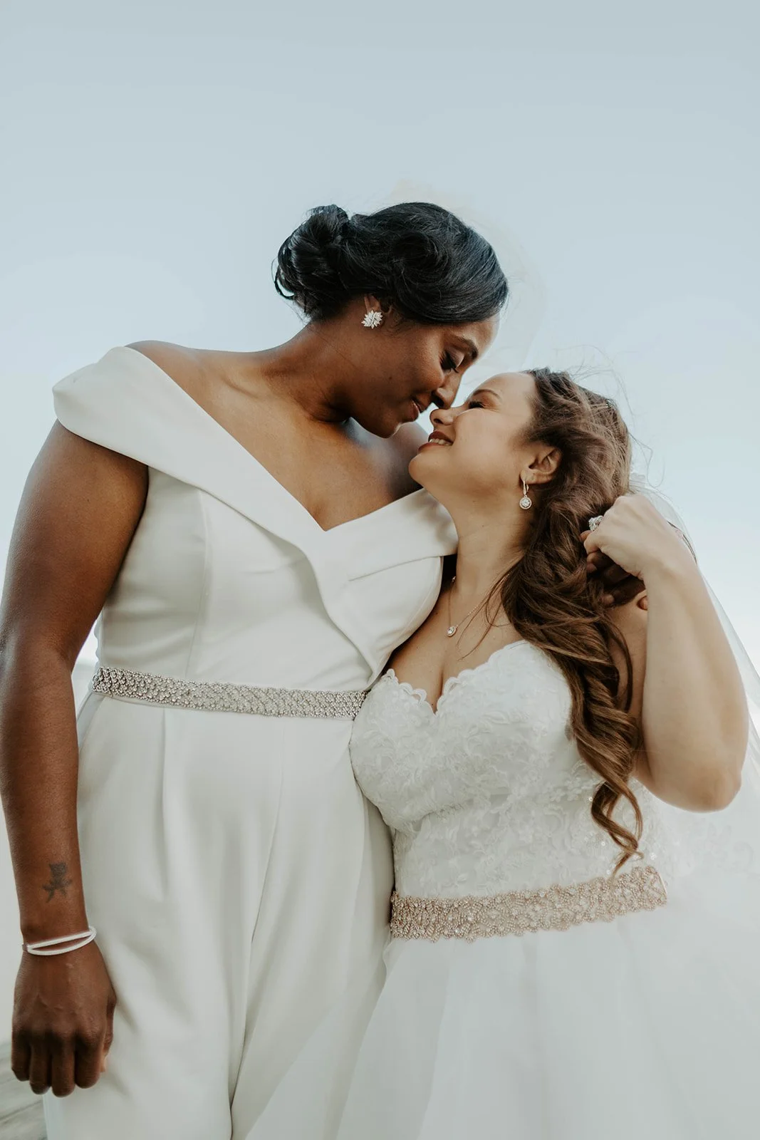 Two brides posing for wedding photos on a dock at Regatta place with the sky behind them