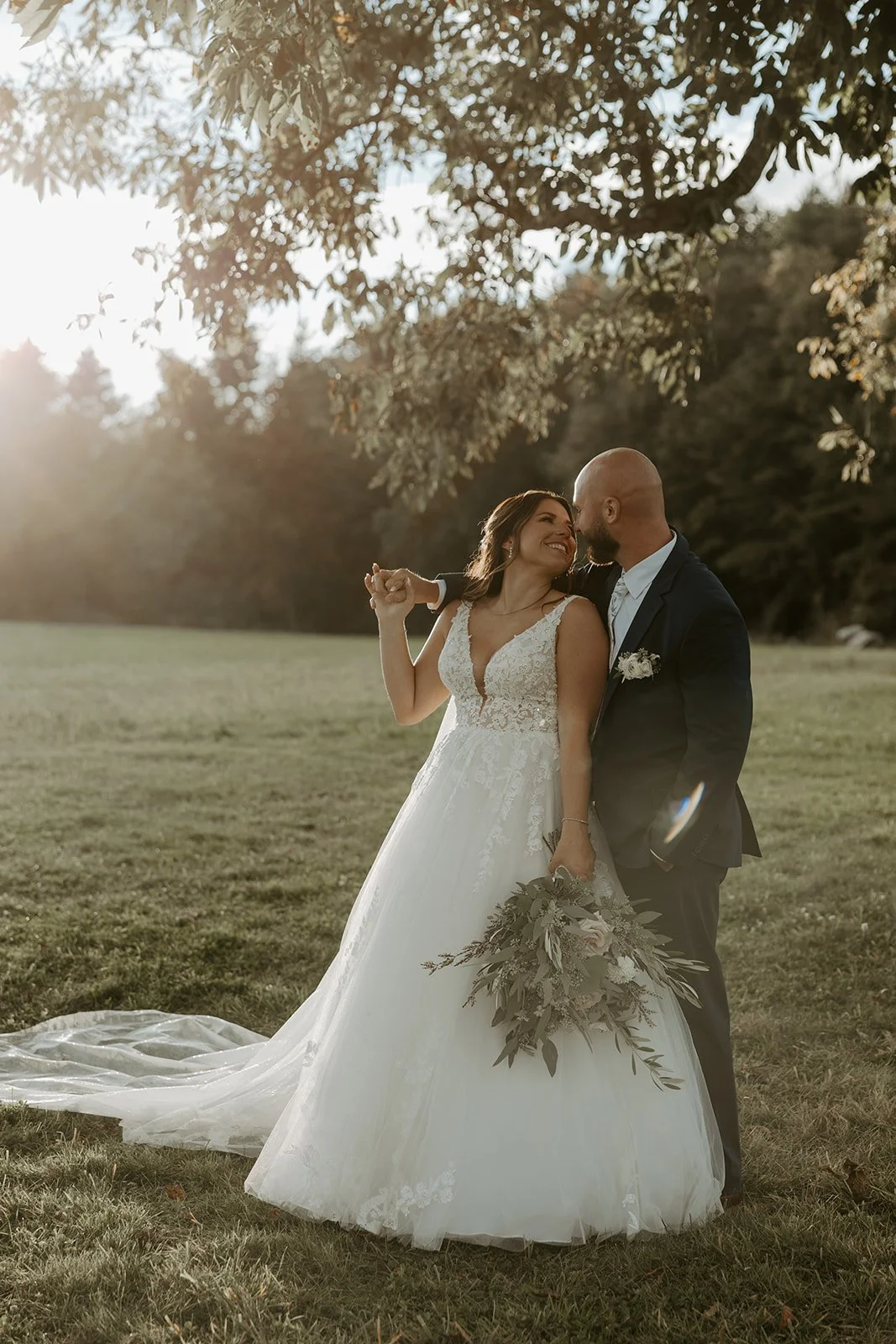 A bride and groom posing for sunset photos on a wide open lawn
