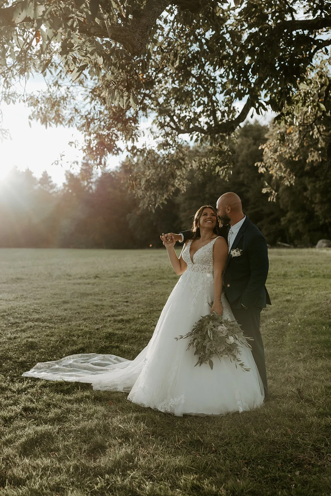 A bride and groom posing for sunset photos on a wide open lawn