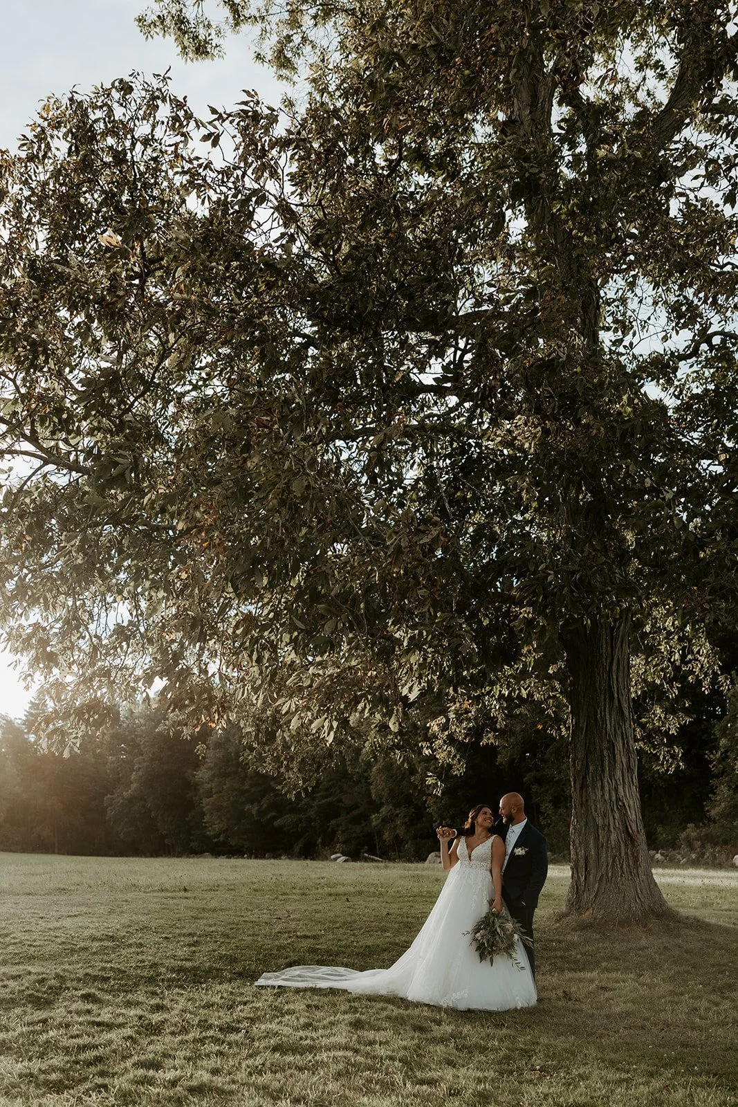 A bride and groom posing for sunset photos on a wide open lawn