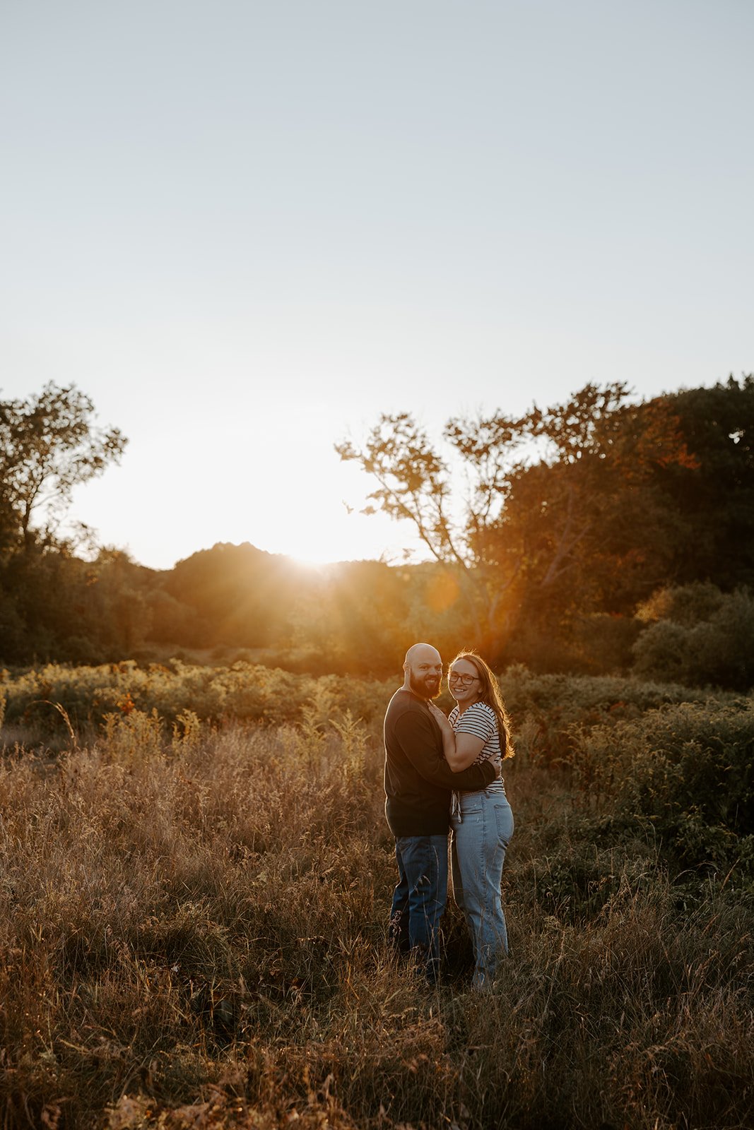 A couple in a field taking sunset engagement photos