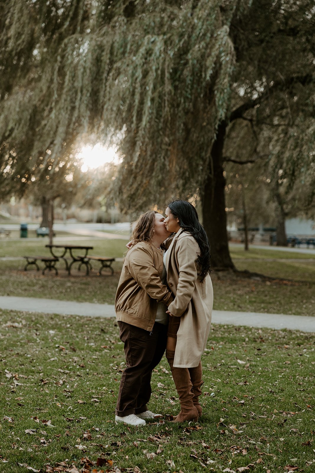 A couple taking engagement photos in front of willow trees at Salem Willows at a Massachusetts engagement photo location