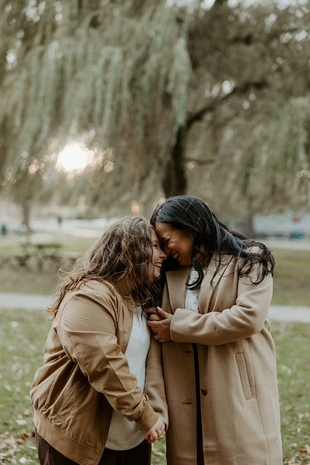 A couple taking engagement photos in front of willow trees at Salem Willows