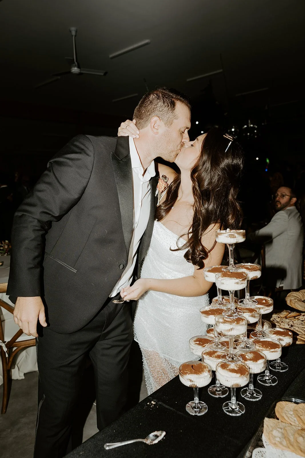 A bride and groom kissing at a tiramisu tower at a backyard wedding