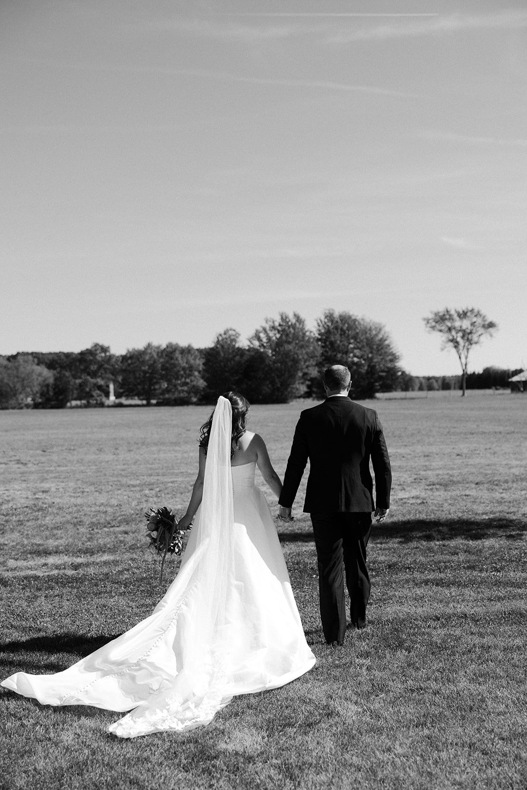 A bride and groom walking away from the camera at their backyard wedding
