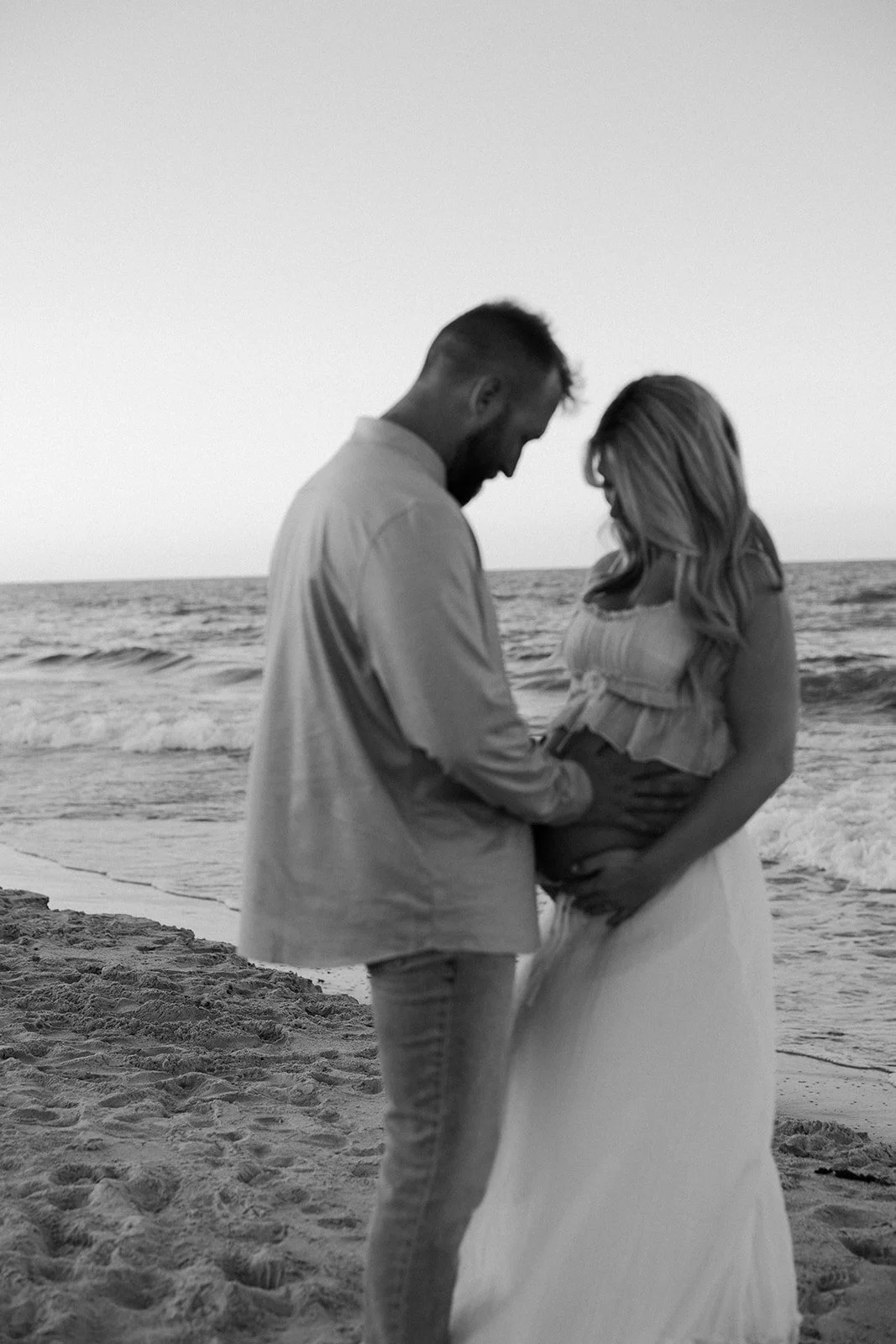A couple taking black and white beach maternity photos