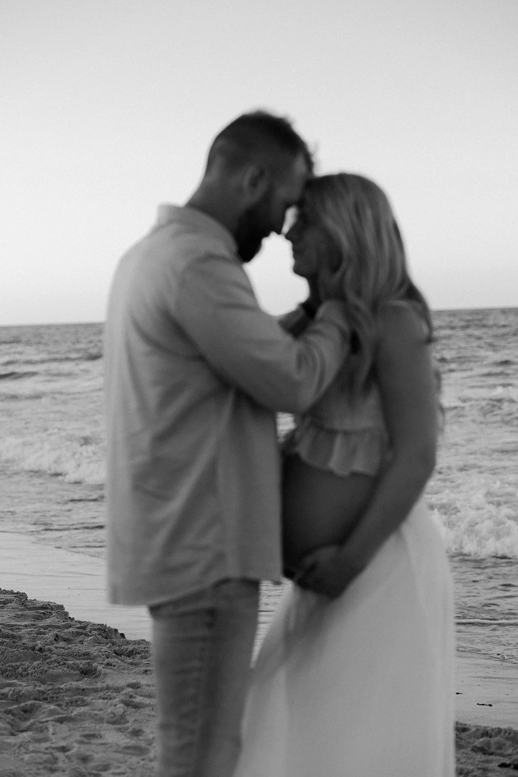 A couple taking black and white beach maternity photos