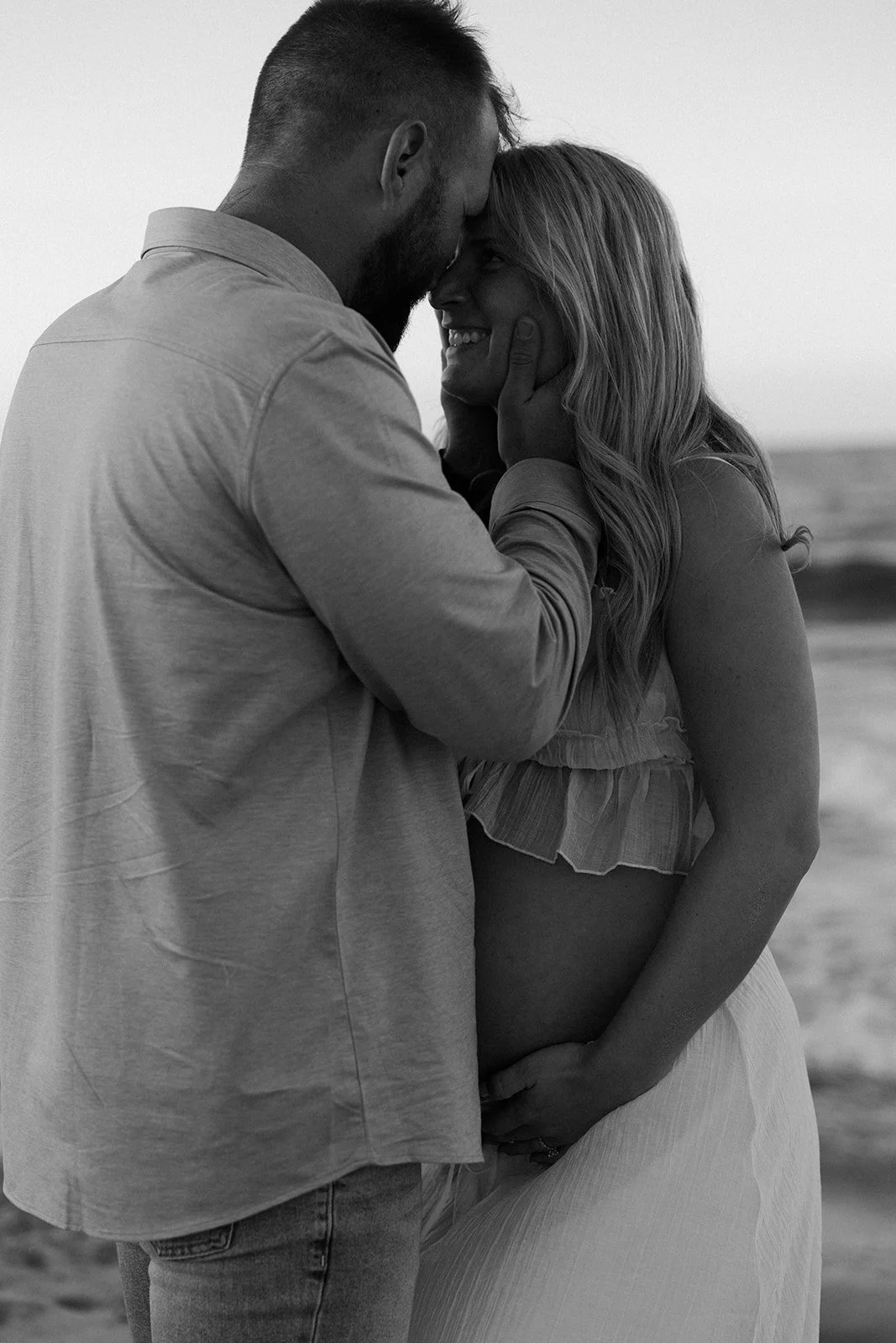 A couple taking black and white beach maternity photos