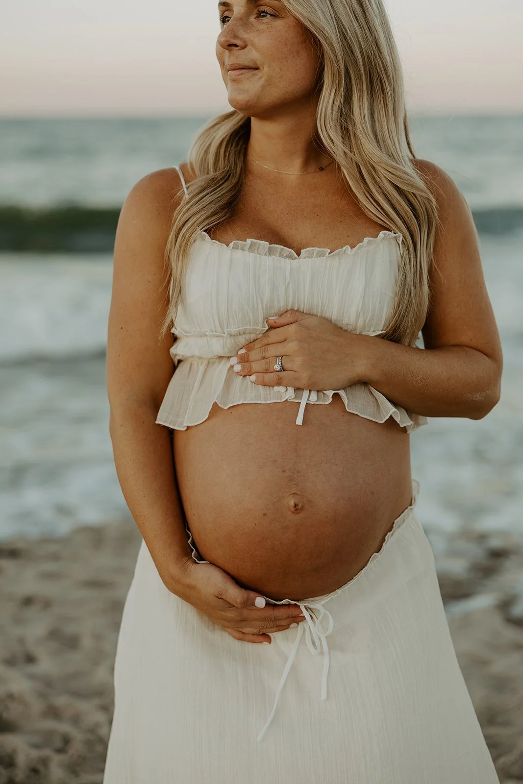 A woman holding her baby bump in a beach maternity photoshoot