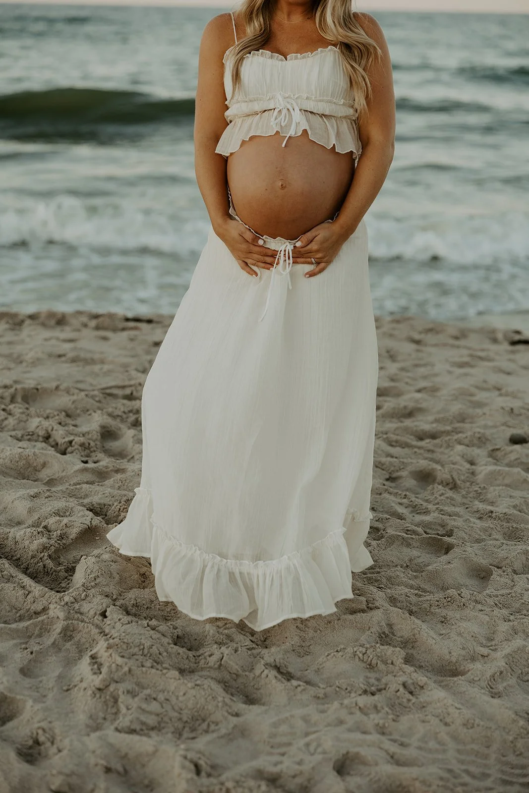 A woman holding her baby bump in a beach photoshoot