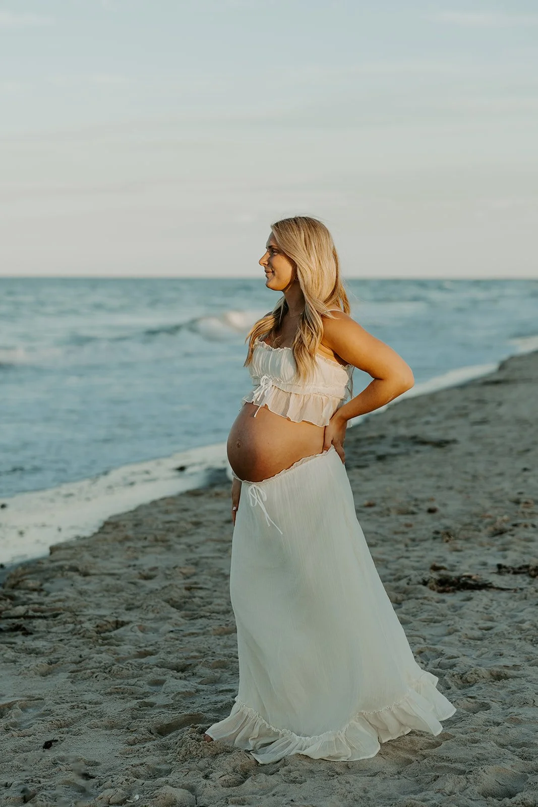 A woman posing for beach maternity photos holding her baby bump
