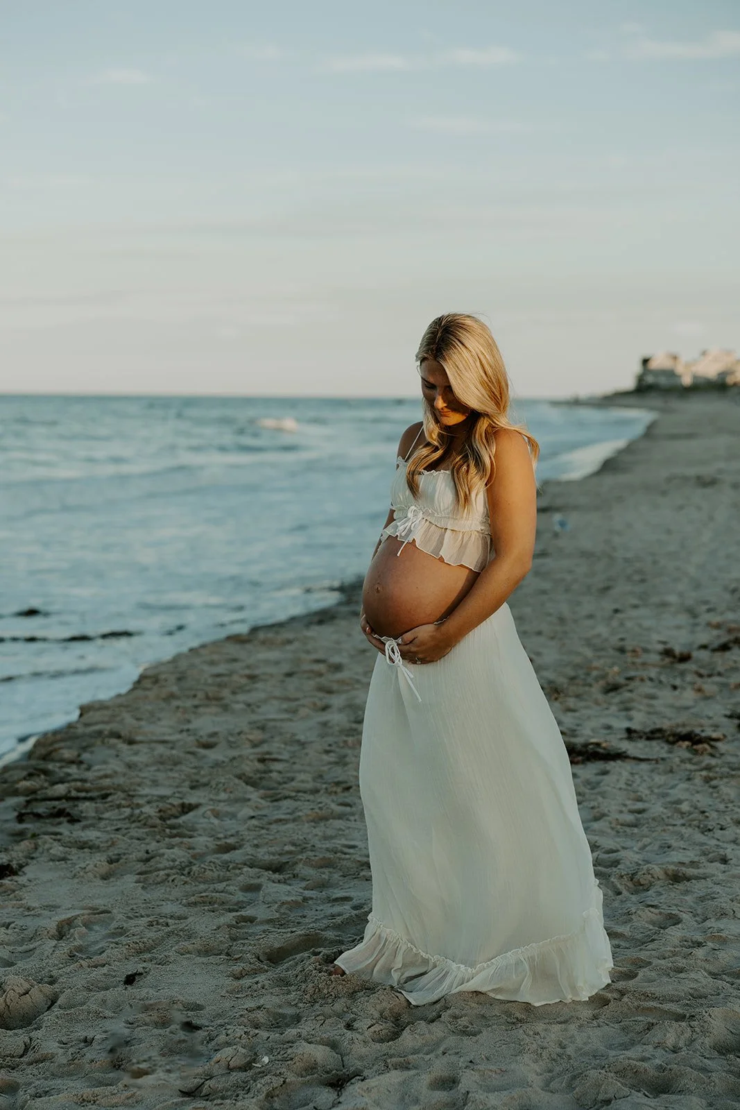 A woman posing for beach maternity photos holding her baby bump