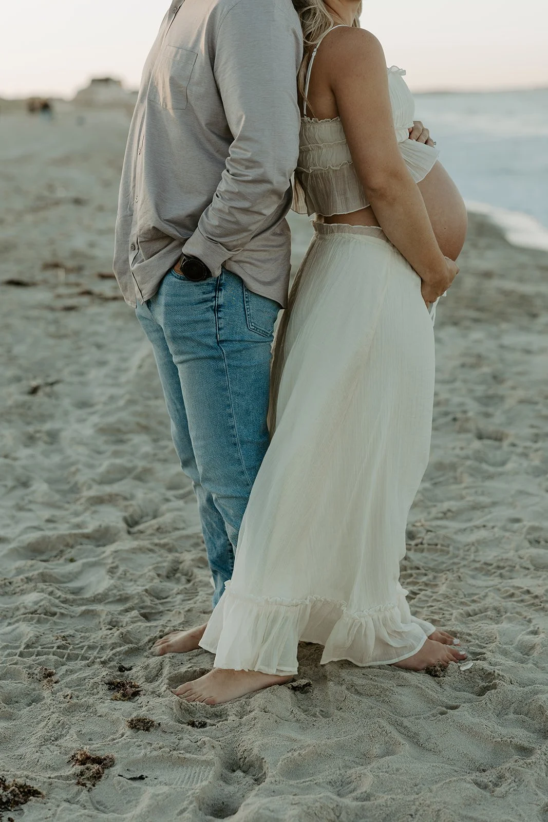 A couple standing back to back for a maternity photoshoot on the beach