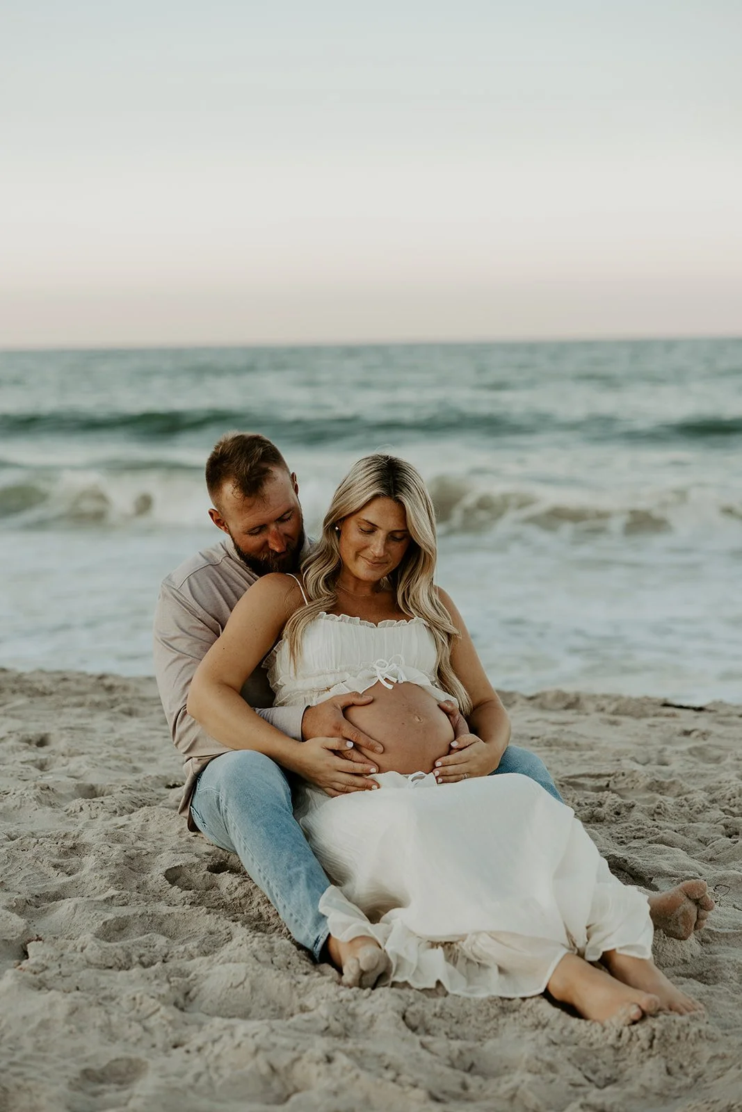 A couple sitting on the beach for maternity photos