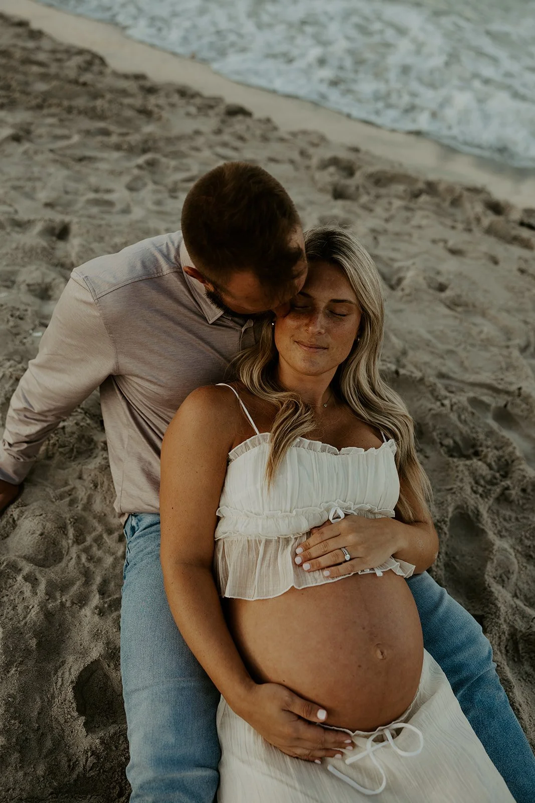 A couple sitting on the beach for maternity photos