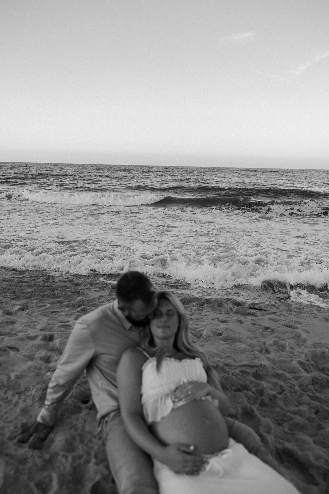 A couple sitting on the beach for maternity photos