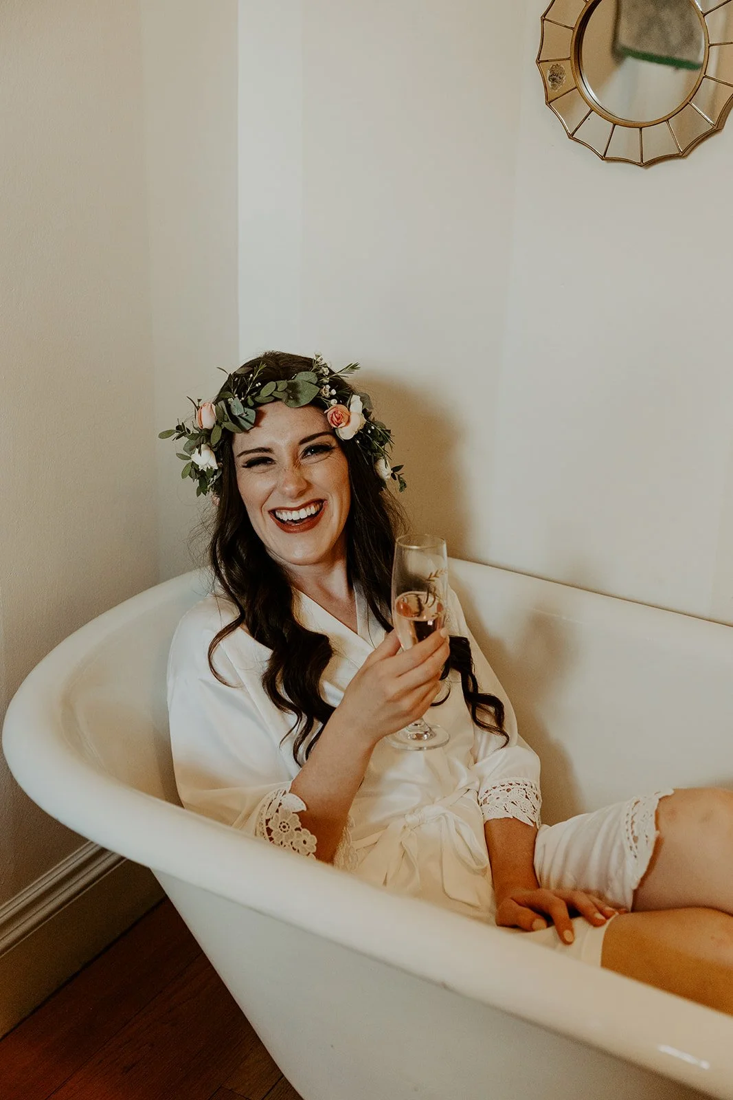 A bride drinking champagne in a bathtub while getting ready for her wedding