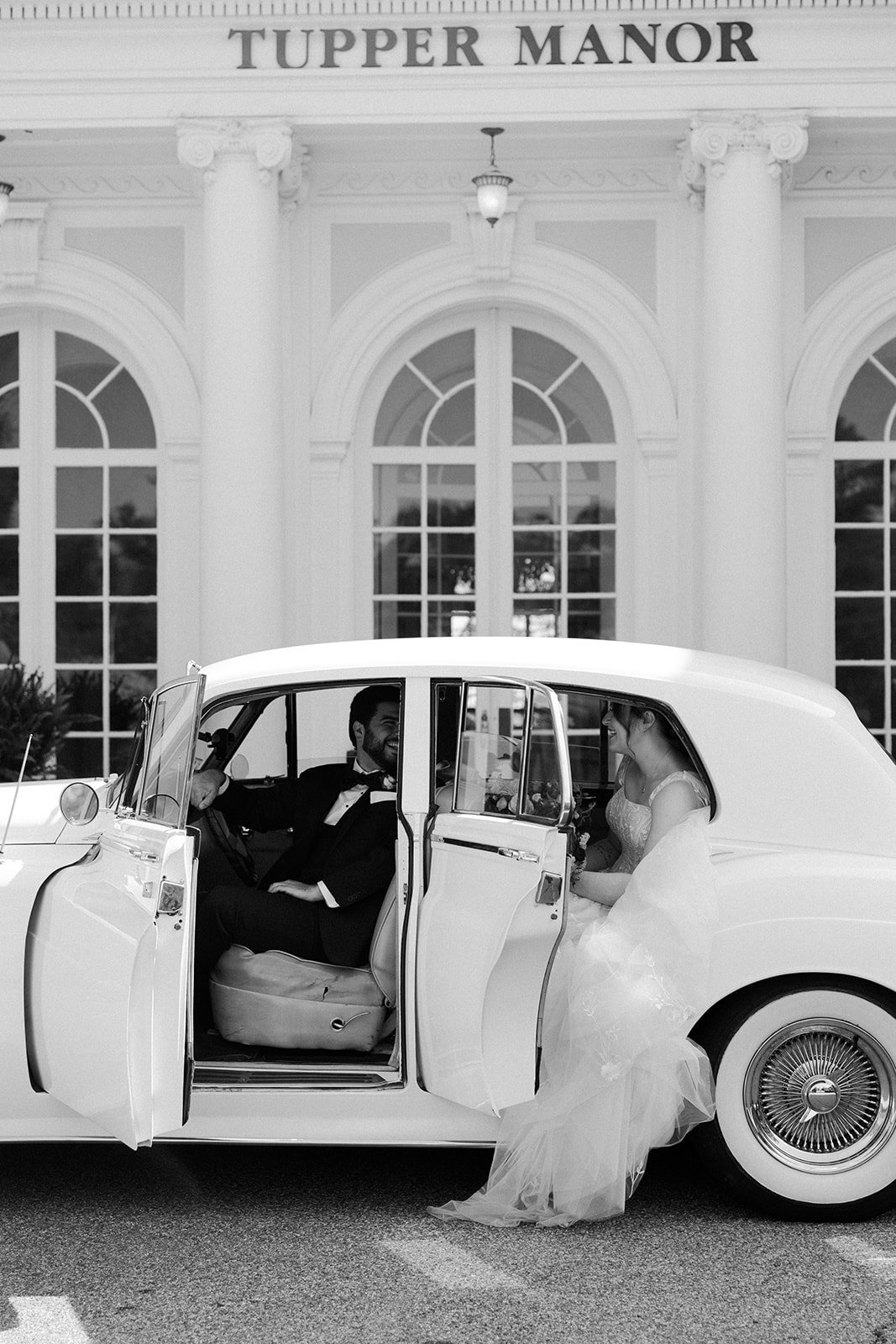 A bride and groom taking photos in a vintage car