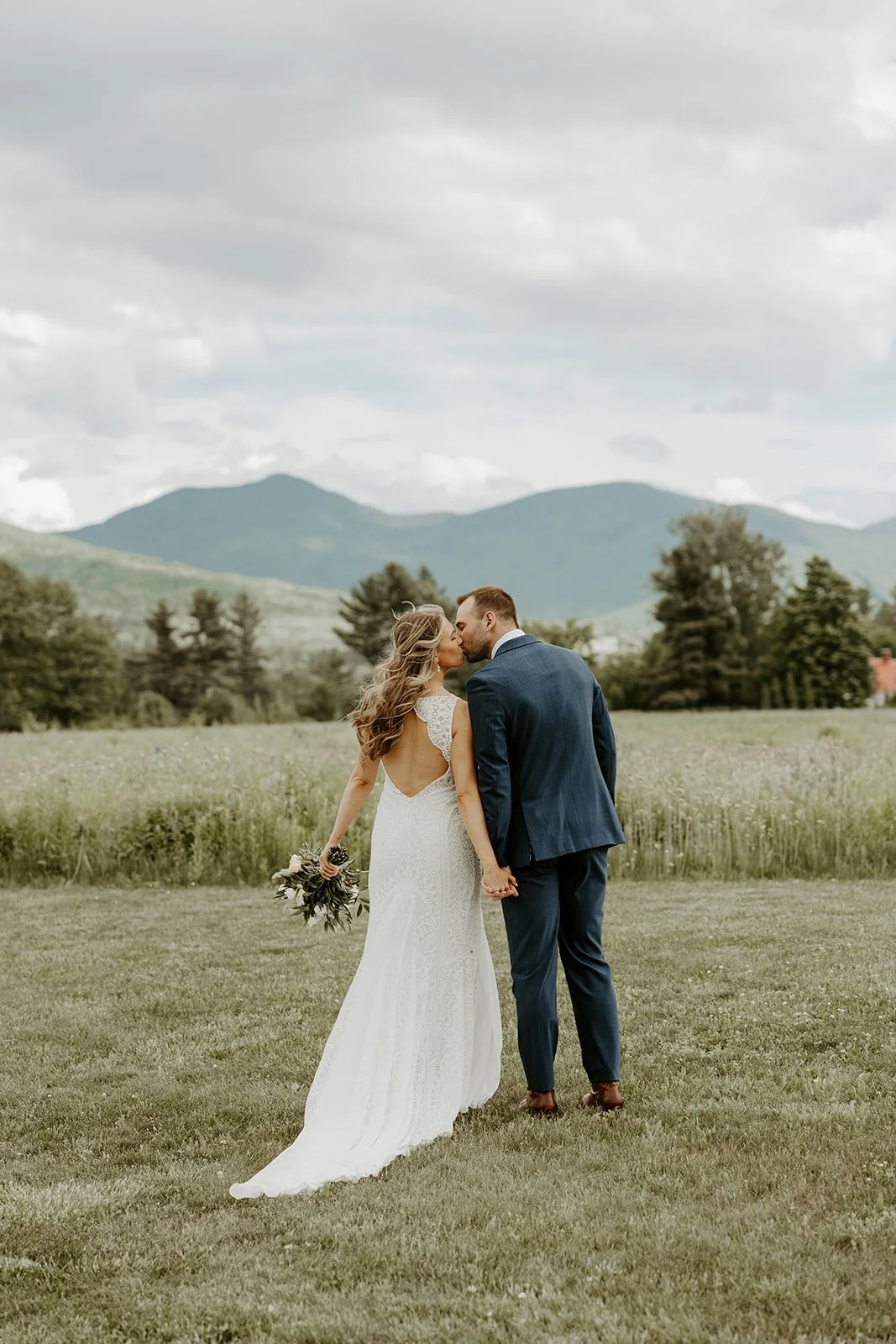 A bride and groom posing for photos in front of the mountains at their Vermont wedding venue