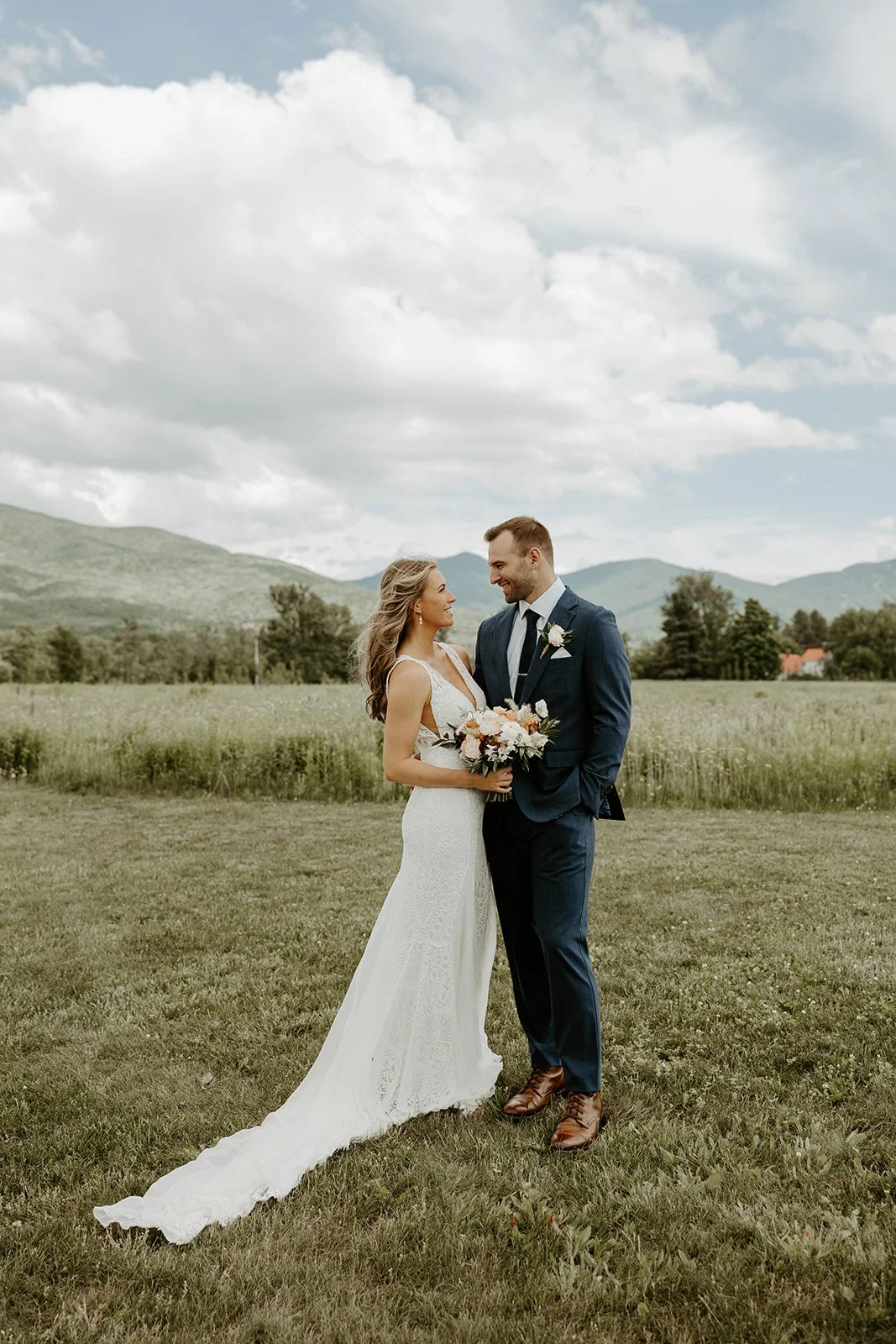 A bride and groom posing for photos in front of the mountains at their Vermont wedding venue