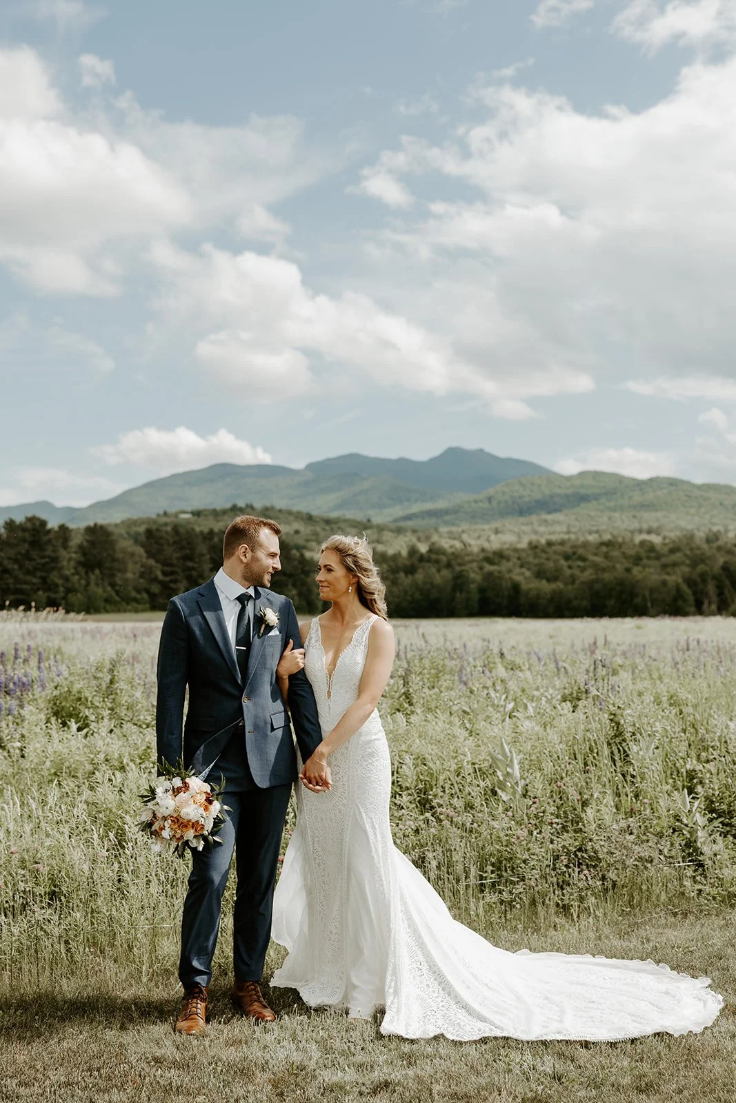 A bride and groom posing for photos in front of the mountains at their Vermont wedding venue