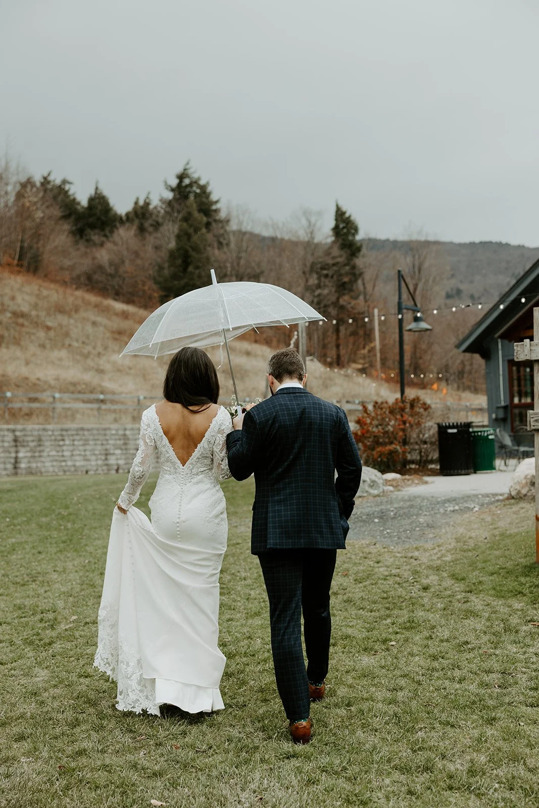 A bride and groom walking at their Vermont wedding venue holding an umbrella