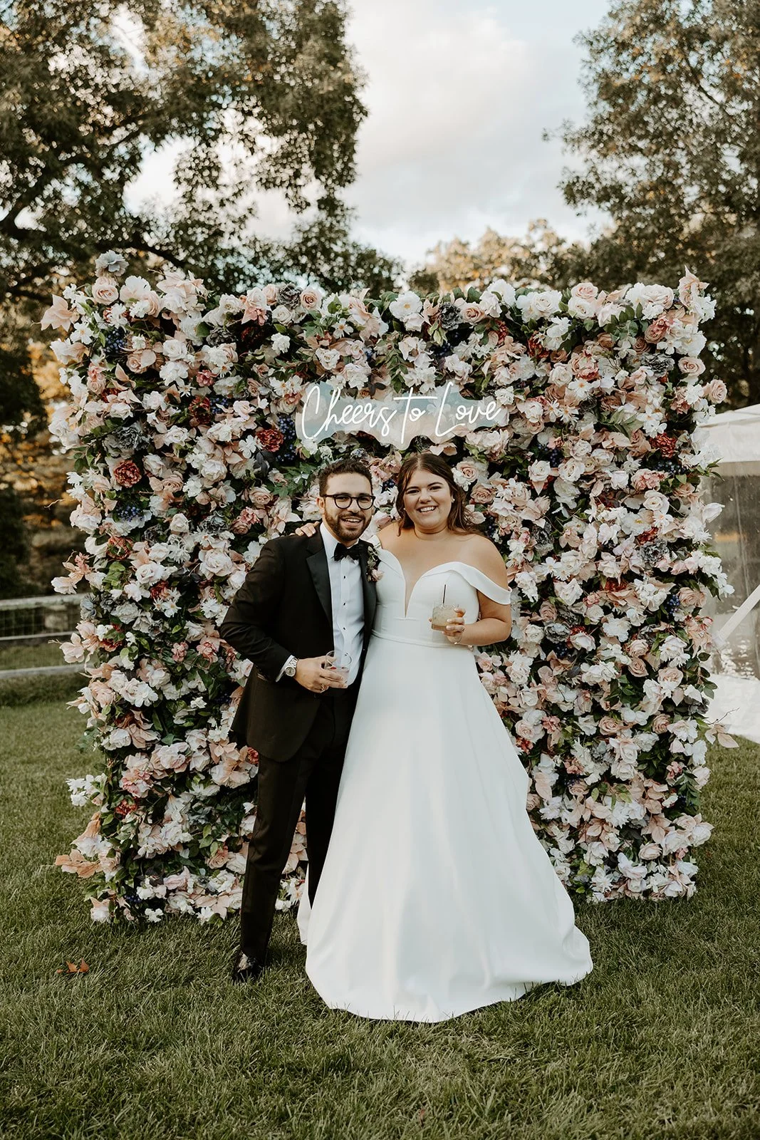 A bride and groom taking photos in front of a flower wall