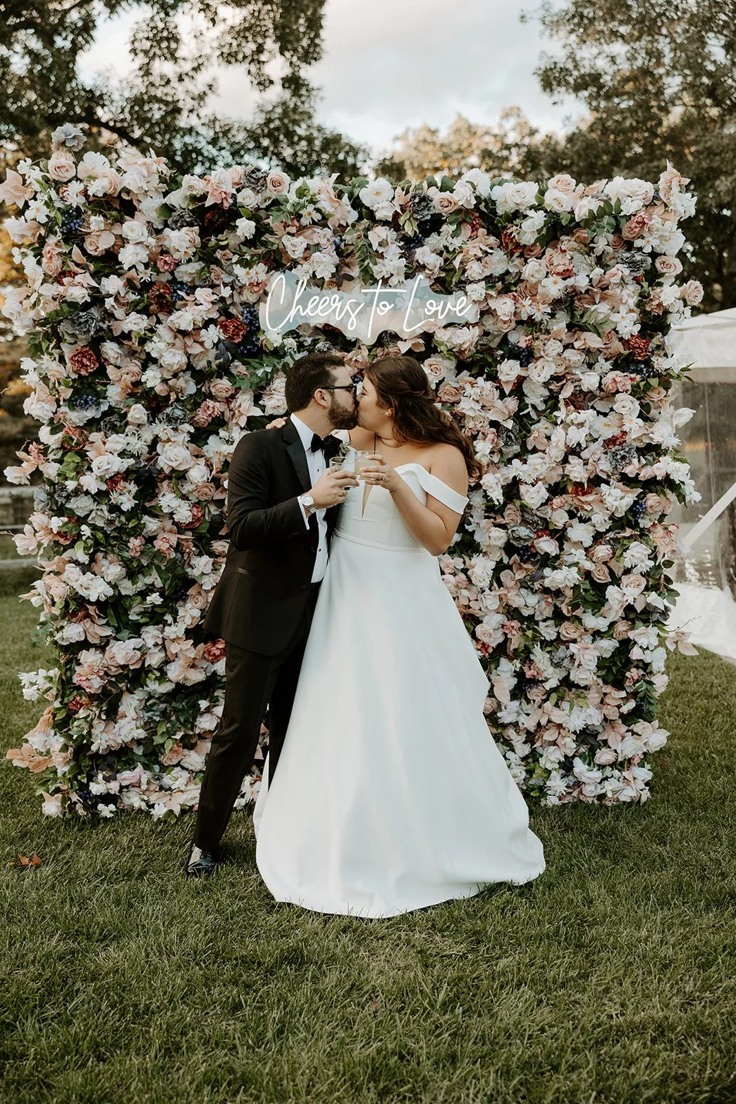 A bride and groom taking photos in front of a flower wall