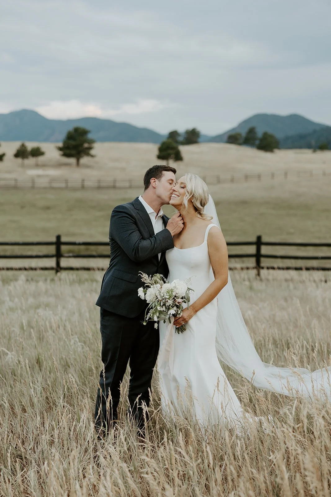 A couple kissing while taking wedding photos in a field